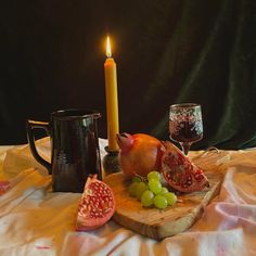 a candle and some fruit are on a wooden board next to a glass of wine