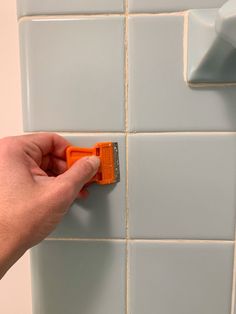 a person is cleaning the tile with a squirt in their hand and an orange sponge on top