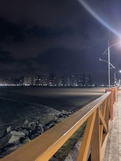 a person walking down a sidewalk next to the ocean at night with city lights in the background