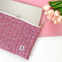 an apple laptop computer sitting on top of a pink flowered bag next to tulips