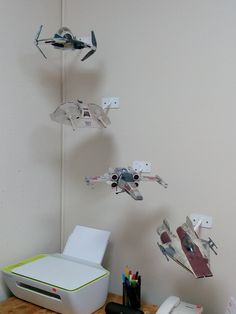 some paper airplanes are hanging on the wall next to a printer and other office supplies