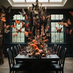 a dining room table is set with black chairs and orange flowers in front of the windows