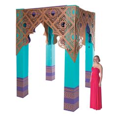 a woman in a red dress standing next to an intricately designed structure with blue columns