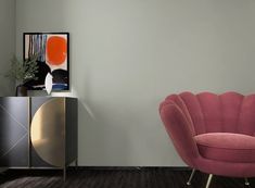 a pink chair sitting in front of a painting on a wall next to a cabinet