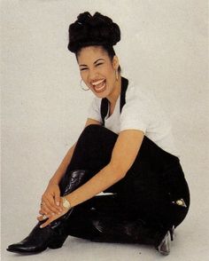 a woman sitting on the ground with her legs crossed, smiling and wearing black shoes