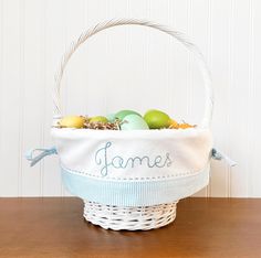 a white basket with some green and yellow eggs in it sitting on a wooden table