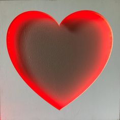 a red heart shaped object on a white wall with light coming from it's center