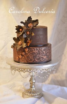 a three tiered cake with chocolate frosting and flowers on top, sitting on a silver stand