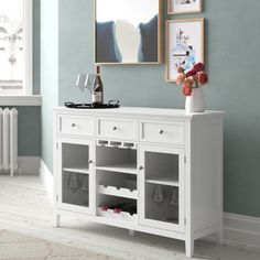 a white sideboard with wine glasses on it in front of a blue painted wall