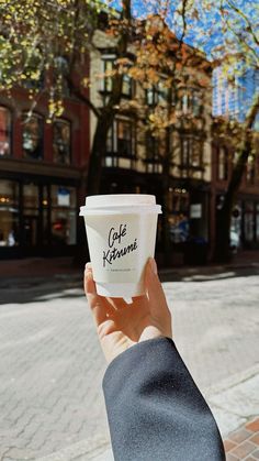 a person holding up a cup of coffee in front of a building on the street