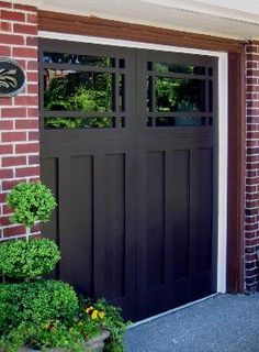 a black garage door with two windows in front of a brick wall and planters on the side