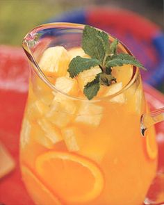 a pitcher filled with oranges and mint on top of a red plate next to sliced lemons