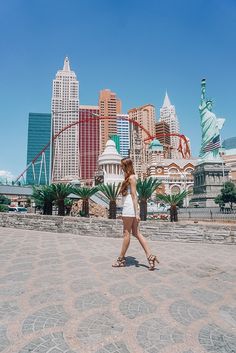 a woman is walking in front of the statue of liberty and las vegas city skyline