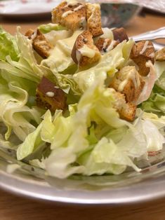 a salad with croutons and dressing on it in a clear glass bowl sitting on a wooden table