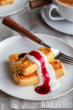 crepes with blueberry sauce and whipped cream are on white plates next to coffee cups