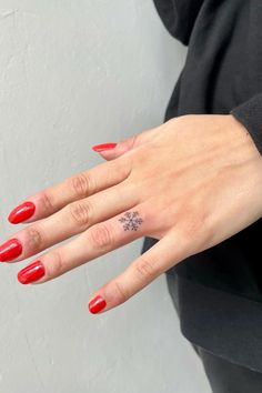 a woman's hand with a small tattoo on her left wrist and red nails