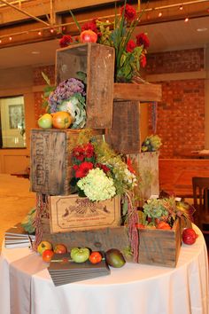 an arrangement of fruits and vegetables on a table in a room with brick walls, white linen