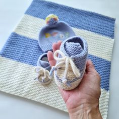 a hand holding a baby bootie on top of a blue and white striped blanket