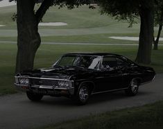 an old black car parked on the side of a road next to trees and grass