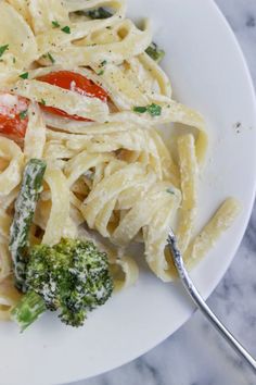 a white plate topped with pasta and broccoli on top of a marble counter