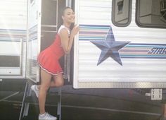 a woman in a red tennis dress leaning against the side of a trailer with a star on it