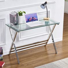 a glass desk with a laptop on it in front of a white wall and wooden floor