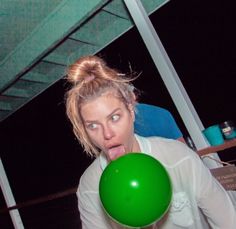 a woman holding a green balloon in front of her face and making a funny face