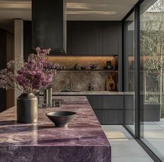 a kitchen with marble counter tops and purple flowers in a vase on the countertop