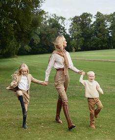 a woman and two children are walking in the grass with their arms around each other