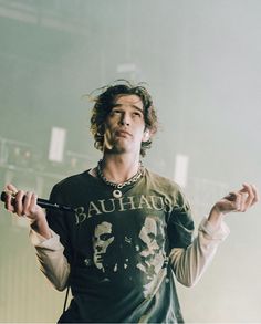 a man with long hair standing in front of a microphone and wearing a black shirt