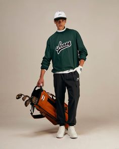 a man in a green sweatshirt holding a baseball bat and glove while standing on a gray background