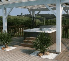 a hot tub sitting on top of a wooden deck next to two potted plants