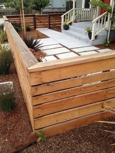 a wooden fence is in the middle of a yard with plants and shrubs around it