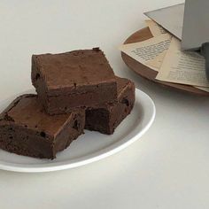 three pieces of brownie on a white plate next to a knife and some books