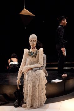 a mannequin sitting on top of a table next to a man in a black suit