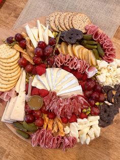 a platter filled with cheese, crackers, grapes and meats on a wooden table