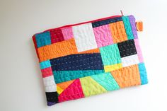 a multicolored patchwork pouch hanging on a wall with an orange hook in the corner