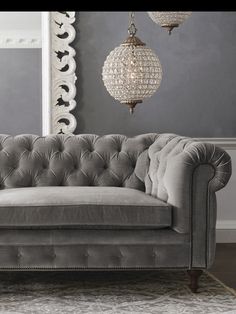 a gray couch in a living room with chandelier hanging from the ceiling and rug on the floor