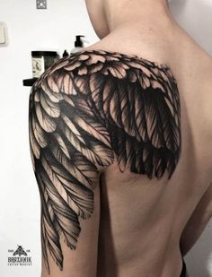 the back of a man's shoulder with an angel wing tattoo on it,