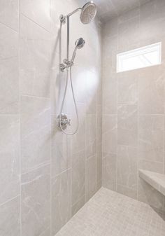 the shower head is mounted on the wall next to the bench in the bathroom, while the light shines through the window