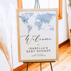 a welcome sign for a baby shower with a world map on the back and an airplane flying over it