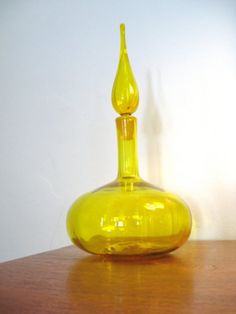 a yellow glass bottle sitting on top of a wooden table next to a white wall