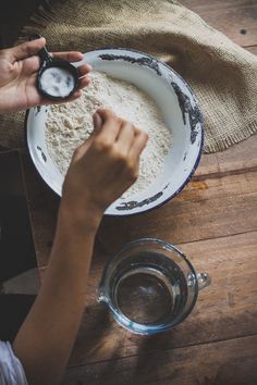 a person holding a spoon over a bowl of food on top of a wooden table