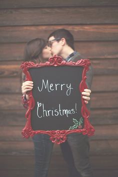 a man and woman kissing in front of a blackboard with merry christmas written on it