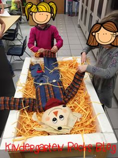 two children standing in front of a fake scarecrow laying on top of some hay