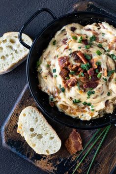 a skillet filled with cheese and bacon on top of a cutting board next to bread