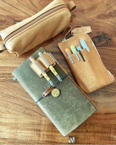 an assortment of pens and pencils are laid out on a wooden table next to a purse