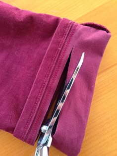 a pair of scissors sitting on top of a piece of purple cloth next to a pair of silverware