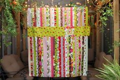 a quilted wall hanging in the middle of a patio with string lights strung above it