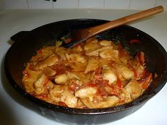 a skillet filled with chicken and vegetables on top of a stove next to a wooden spoon